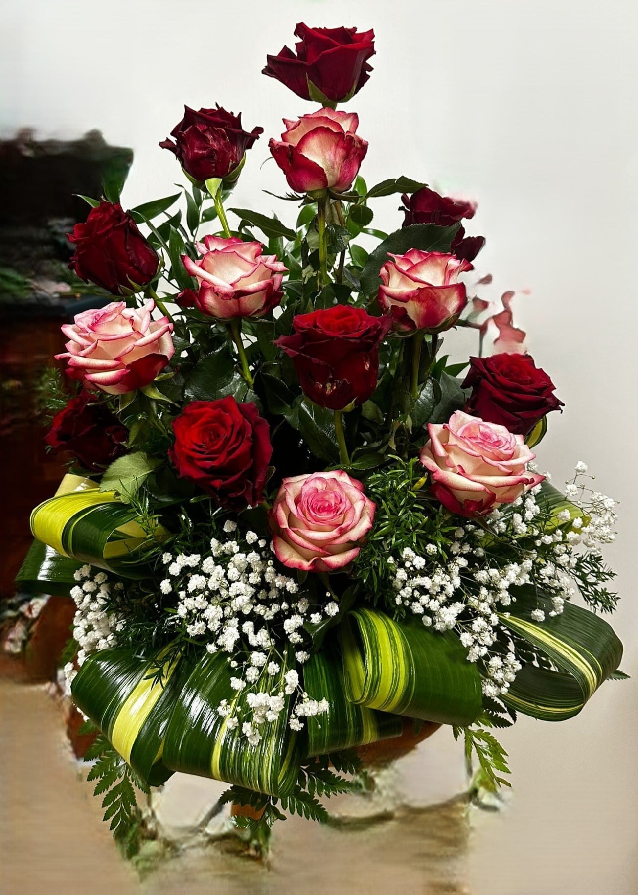 Composizione in ciotola con rose di vari colori e foglie decorative, misura media, elegante per tombe o omaggi commemorativi.
