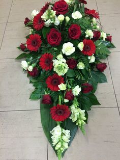 Elegante cofano funebre metà misura con rose e gerbere rosse e fiori bianchi freschi. Nastro personalizzabile. Perfetto come decorazione per bara o omaggio floreale moderno.