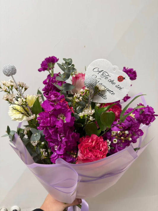 Bouquet di fiori freschi di stagione con cuore decorativo e frasi personalizzabili, confezionato con materiale idrorepellente e fiocco elegante.