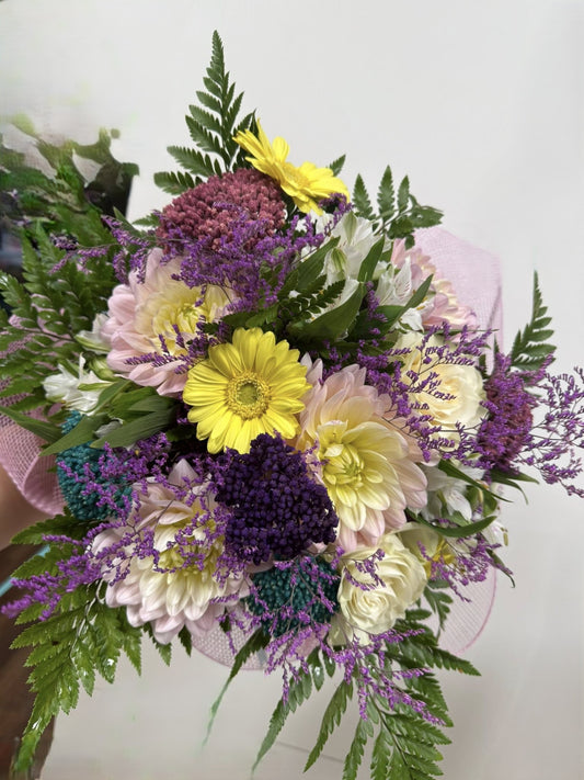 Bouquet di fiori freschi di stagione in giallo, lilla e viola con incarto elegante e fiocco abbinato.