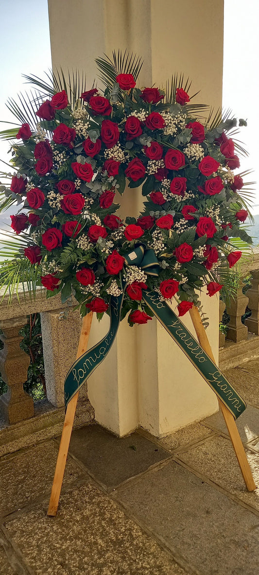 Corona funebre elegante con rose rosse, simbolo di amore eterno e rispetto. Diametro standard 140 cm, disponibile anche versione da 100 cm. Nastro personalizzabile con dedica.