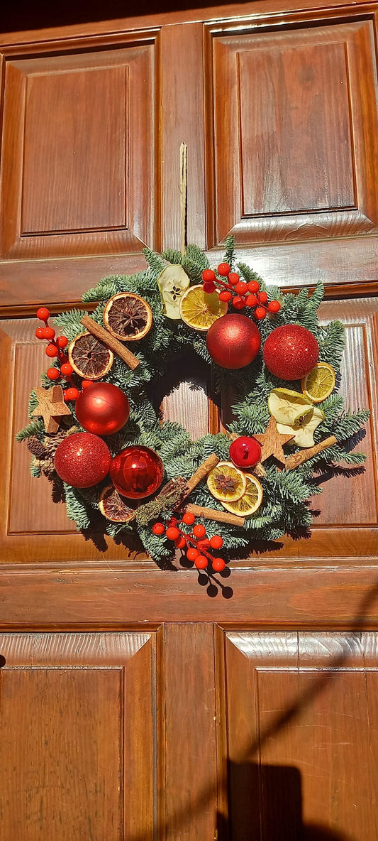Ghirlanda natalizia artigianale di pino fresco, decorata con arance essiccate, cannella, bacche naturali e palline colorate. Raggio circa 35-40 cm, ideale per porte, pareti o centrotavola, con autentico profumo di Natale.
